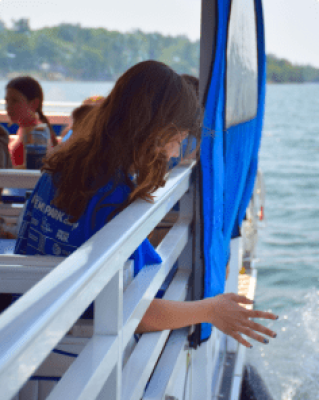 A young student reaches for the St. Lawrence from the side of a field trip boat.